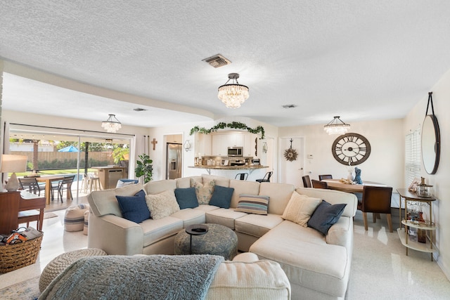 living area with a textured ceiling, visible vents, light speckled floor, and a notable chandelier