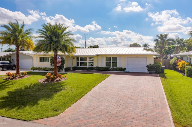 ranch-style house featuring a garage, metal roof, decorative driveway, a front yard, and stucco siding