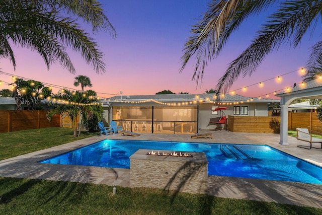 pool at dusk with a patio area, a fenced backyard, and a fire pit