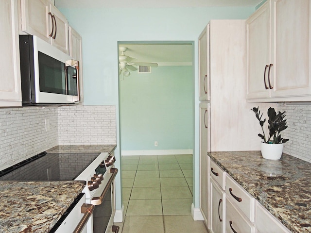 kitchen with light tile floors, ceiling fan, appliances with stainless steel finishes, backsplash, and dark stone countertops