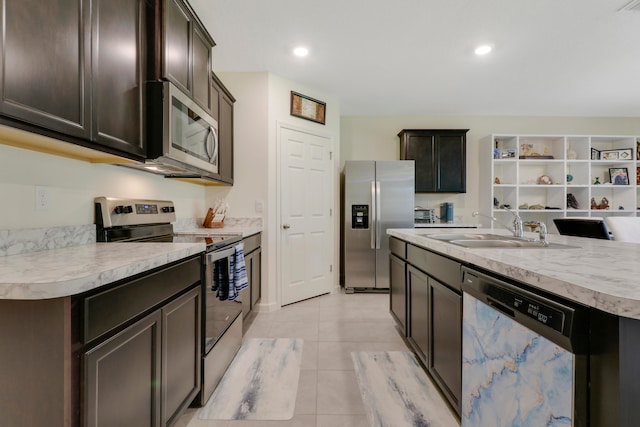 kitchen with appliances with stainless steel finishes, dark brown cabinets, a kitchen island with sink, sink, and light tile flooring