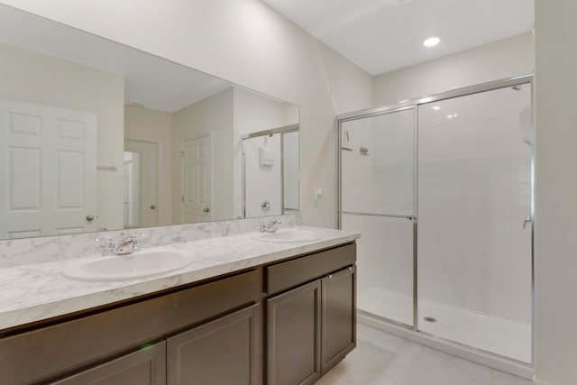 bathroom with a shower with shower door, dual sinks, tile floors, and vanity with extensive cabinet space