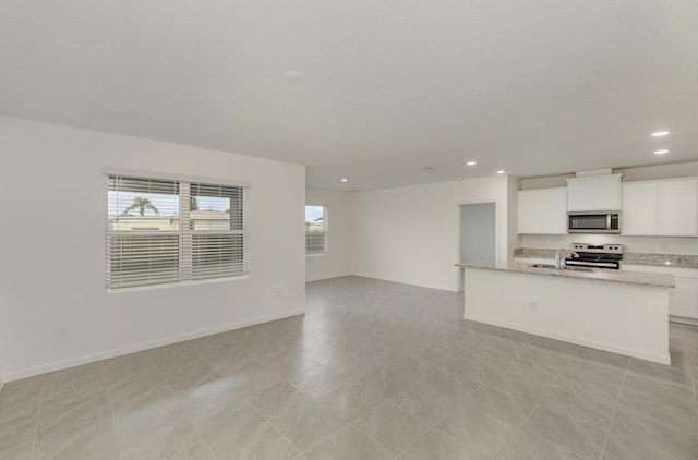 kitchen with appliances with stainless steel finishes, a center island with sink, white cabinetry, and light tile patterned floors