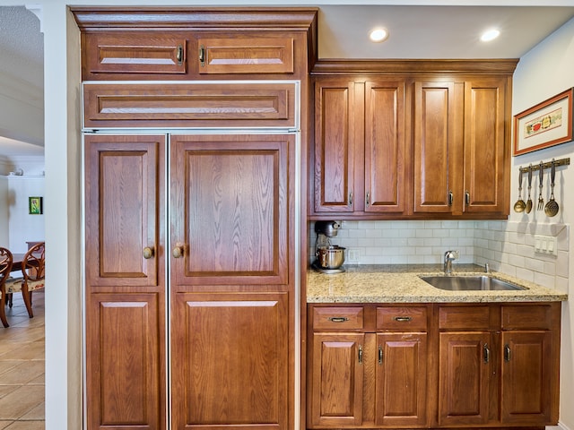 kitchen featuring tasteful backsplash, light tile floors, sink, and light stone countertops