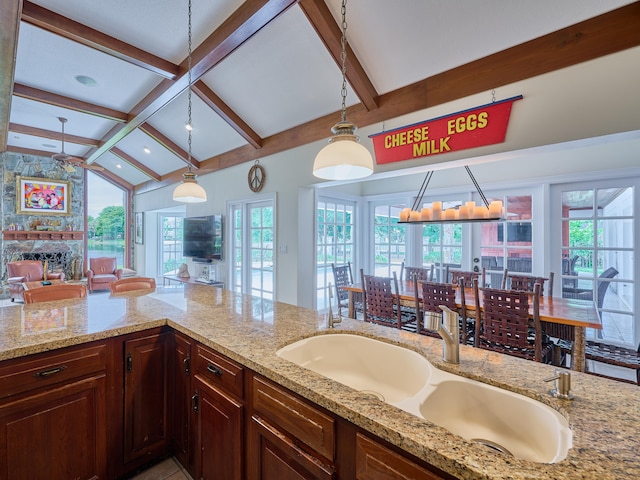 kitchen with plenty of natural light, light stone countertops, vaulted ceiling with beams, and decorative light fixtures