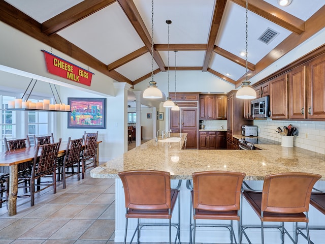 kitchen featuring light stone countertops, hanging light fixtures, a breakfast bar area, tasteful backsplash, and sink