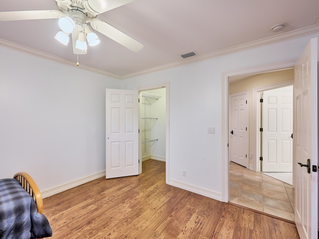 unfurnished bedroom with a closet, ceiling fan, light tile floors, a walk in closet, and crown molding