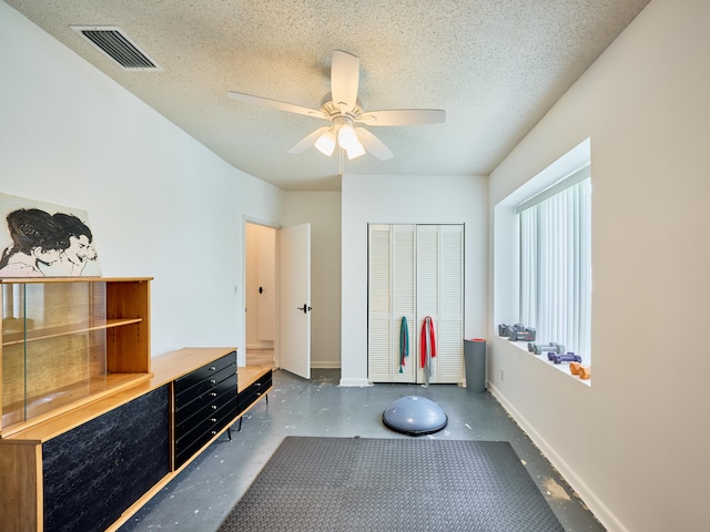 exercise area featuring ceiling fan and a textured ceiling