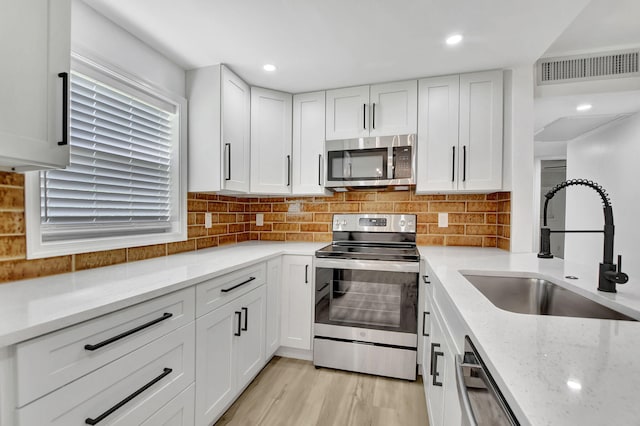 kitchen featuring white cabinets, light wood-type flooring, light stone countertops, and appliances with stainless steel finishes