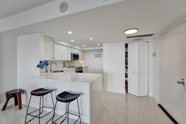 kitchen with backsplash, stainless steel appliances, sink, a kitchen bar, and light tile floors