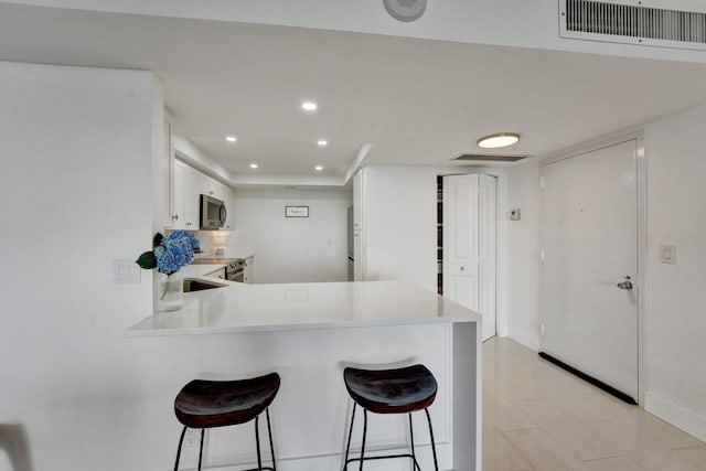 kitchen featuring kitchen peninsula, white cabinetry, a breakfast bar area, and light tile flooring