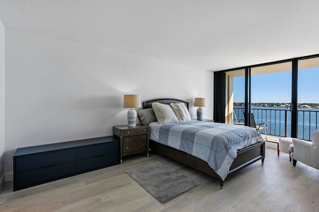 bedroom featuring a water view, floor to ceiling windows, and light hardwood / wood-style flooring