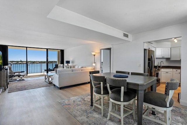 dining area featuring a water view, sink, light hardwood / wood-style floors, and expansive windows