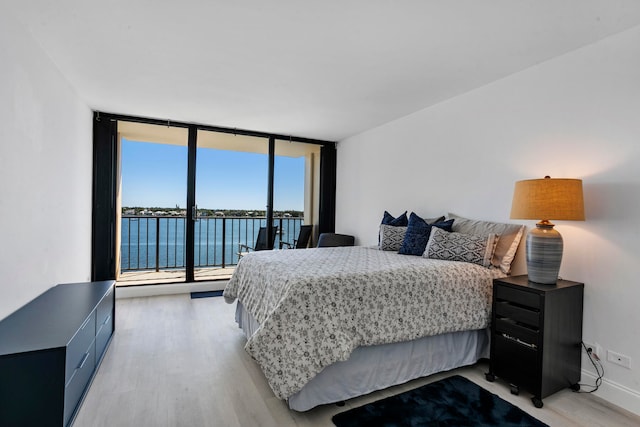 bedroom with a water view, expansive windows, and light hardwood / wood-style flooring