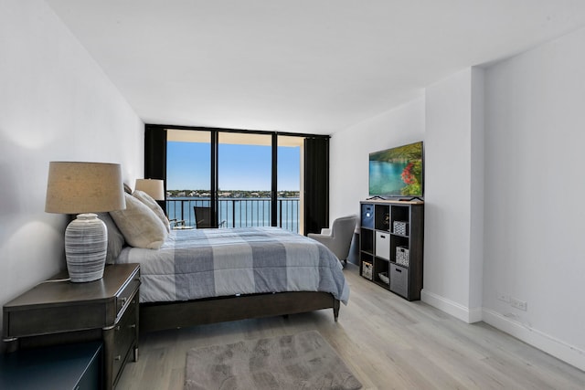 bedroom featuring light hardwood / wood-style flooring, a wall of windows, and a water view