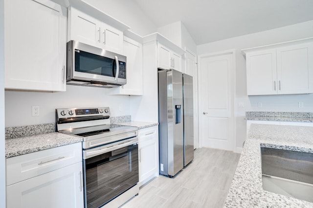 kitchen featuring lofted ceiling, stainless steel appliances, sink, light stone countertops, and white cabinets