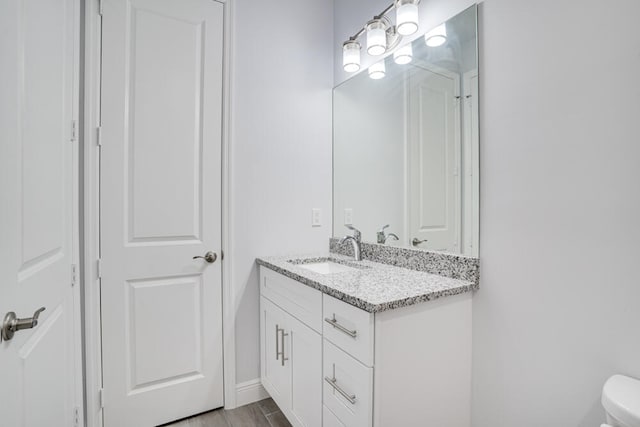 bathroom featuring toilet, vanity with extensive cabinet space, and wood-type flooring