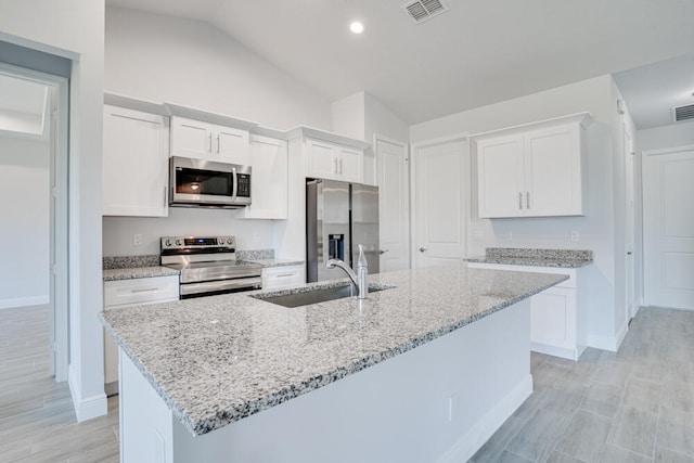 kitchen with an island with sink, white cabinets, stainless steel appliances, vaulted ceiling, and light stone countertops