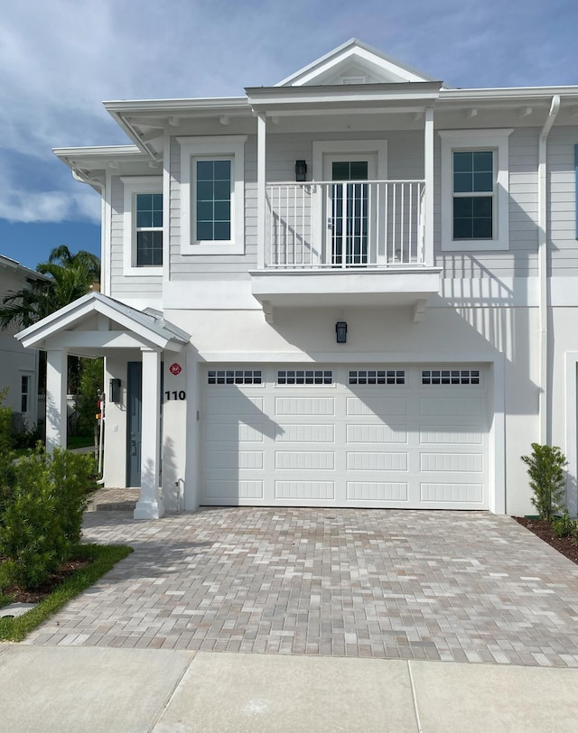 view of front of home featuring stucco siding, an attached garage, a balcony, and decorative driveway