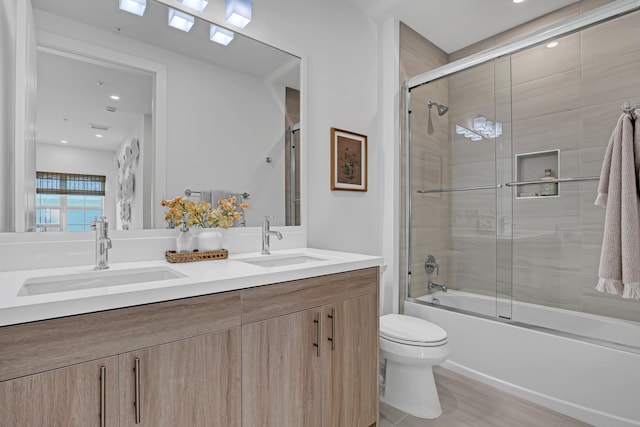 full bath featuring shower / bath combination with glass door, double vanity, a sink, and toilet