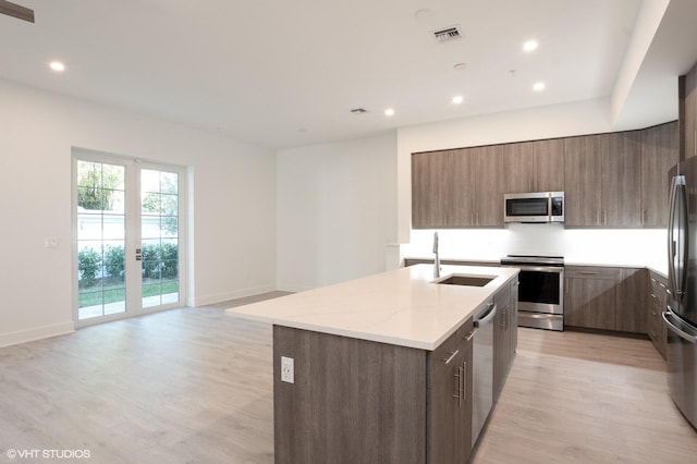 kitchen with french doors, a center island with sink, sink, light hardwood / wood-style floors, and stainless steel appliances