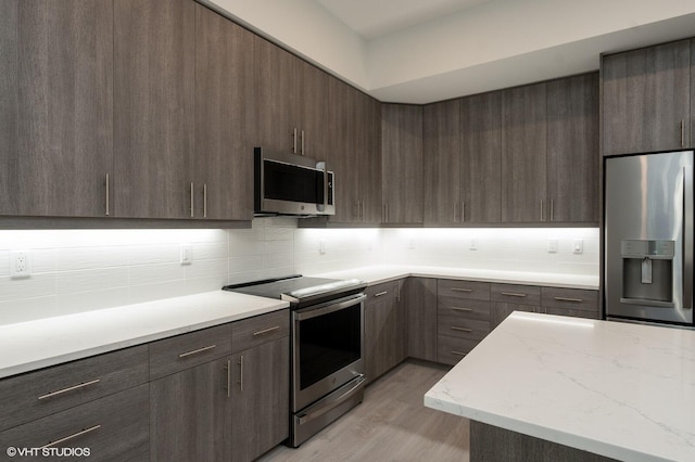 kitchen with dark brown cabinets, light hardwood / wood-style floors, decorative backsplash, and appliances with stainless steel finishes