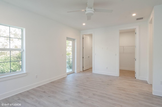 unfurnished bedroom with a walk in closet, ceiling fan, multiple windows, and light wood-type flooring