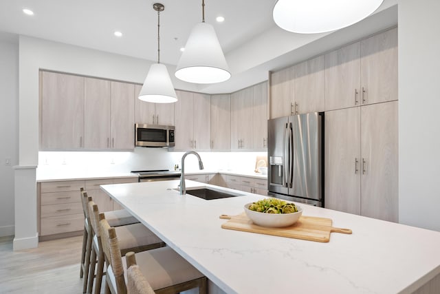 kitchen with appliances with stainless steel finishes, light brown cabinets, a center island with sink, and sink