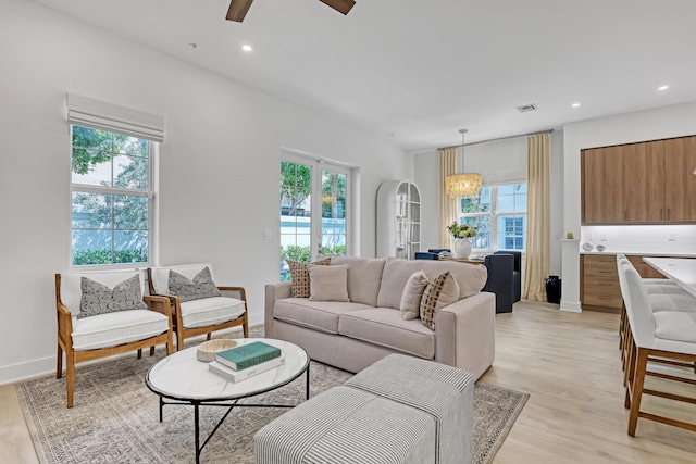living area featuring light wood-style floors, ceiling fan with notable chandelier, visible vents, and a healthy amount of sunlight