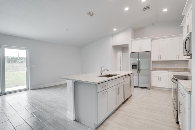 kitchen with white cabinets, stainless steel appliances, a kitchen island with sink, sink, and vaulted ceiling