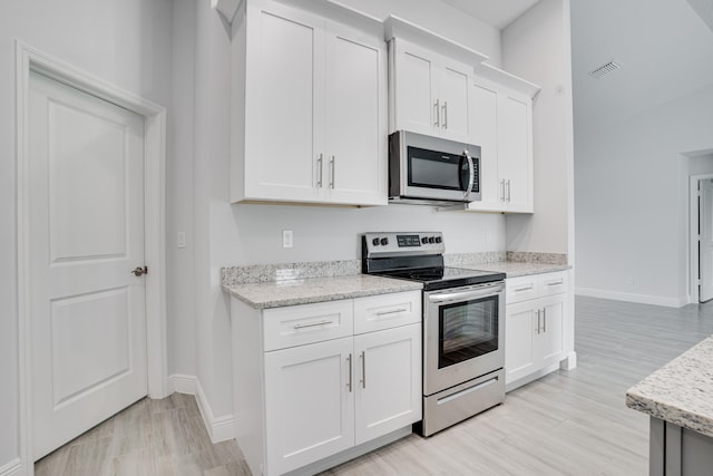 kitchen with stainless steel appliances, light stone counters, and white cabinets