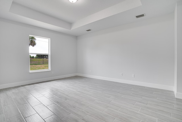 empty room featuring light wood-type flooring and a raised ceiling