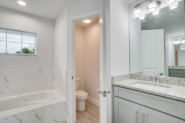 bathroom featuring hardwood / wood-style flooring, toilet, vanity, and a relaxing tiled bath