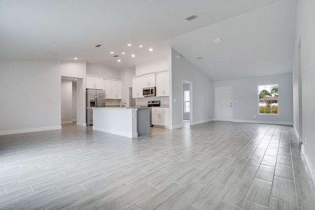 kitchen with white cabinetry, appliances with stainless steel finishes, high vaulted ceiling, light hardwood / wood-style flooring, and an island with sink