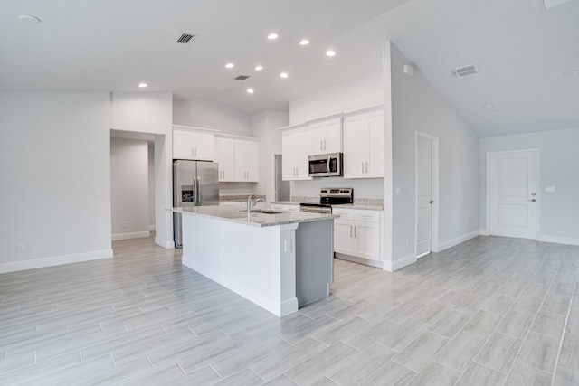 kitchen featuring white cabinets, appliances with stainless steel finishes, a center island with sink, light stone countertops, and high vaulted ceiling