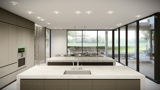 kitchen featuring a wall of windows, light stone countertops, modern cabinets, a center island with sink, and a sink