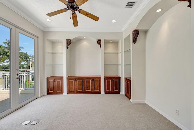 carpeted spare room with french doors, ceiling fan, built in features, and ornamental molding