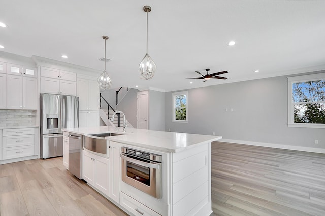 kitchen featuring white cabinetry, sink, backsplash, a kitchen island with sink, and appliances with stainless steel finishes