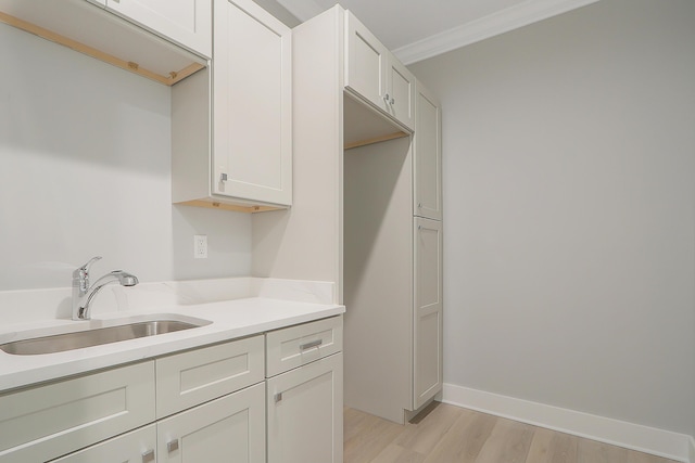 kitchen featuring light hardwood / wood-style flooring, white cabinetry, ornamental molding, and sink