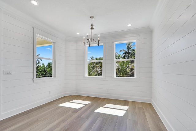 unfurnished dining area with wood walls, a notable chandelier, light hardwood / wood-style floors, and crown molding