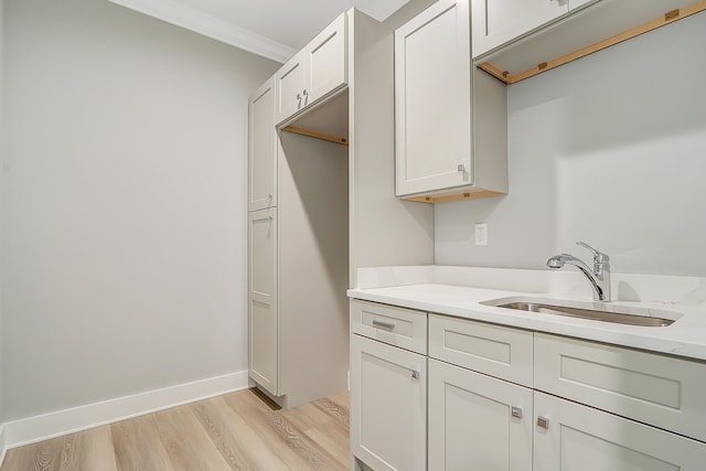 kitchen featuring light stone countertops, ornamental molding, sink, light hardwood / wood-style flooring, and white cabinetry