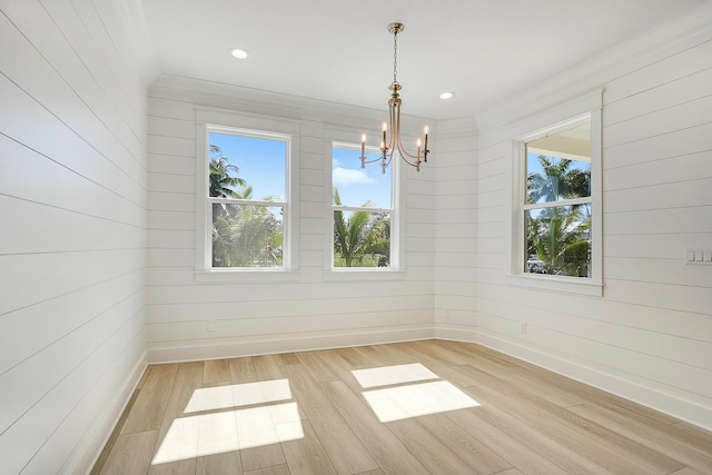 unfurnished dining area featuring a notable chandelier, a healthy amount of sunlight, light wood-type flooring, and wooden walls