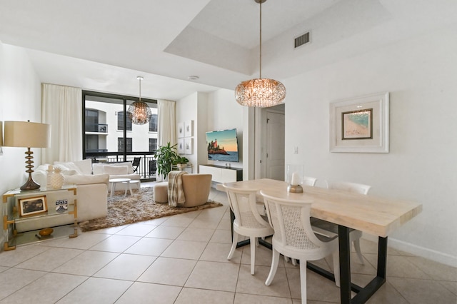 dining area with a raised ceiling, an inviting chandelier, and light tile flooring