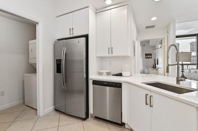 kitchen featuring stacked washer / dryer, stainless steel appliances, light tile floors, sink, and white cabinets