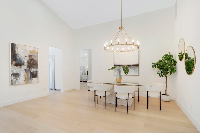 dining area with a notable chandelier, light hardwood / wood-style floors, and a high ceiling