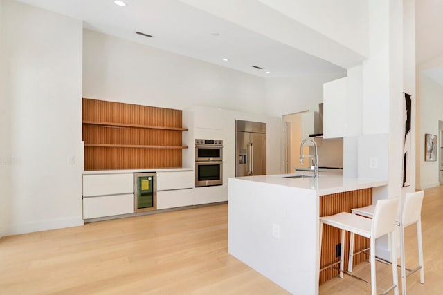 kitchen featuring stainless steel appliances, light hardwood / wood-style floors, a high ceiling, white cabinets, and a kitchen breakfast bar