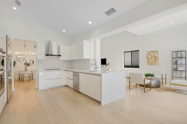 kitchen with light wood-type flooring, wall chimney range hood, a chandelier, and white cabinetry