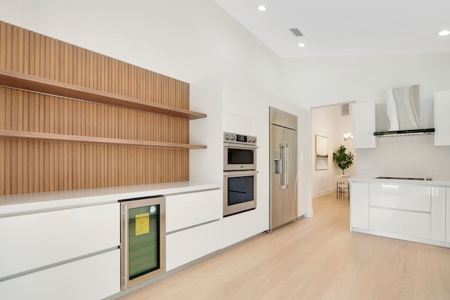 kitchen with white cabinets, wine cooler, light hardwood / wood-style floors, wall chimney range hood, and stainless steel appliances