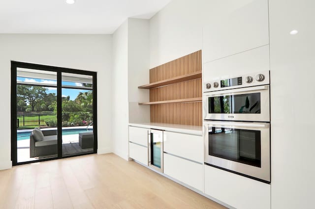 kitchen with beverage cooler, white cabinets, lofted ceiling, stainless steel double oven, and light hardwood / wood-style flooring