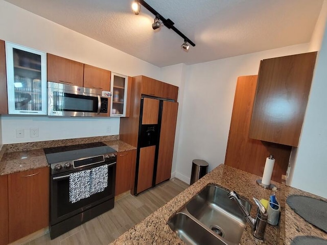 kitchen featuring fridge with ice dispenser, electric range, rail lighting, stone counters, and sink